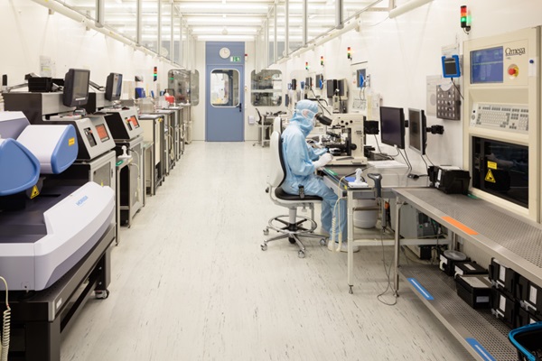 Reinraum-Fertigung. Mensch in Schutzanzug an einem Mikroskop